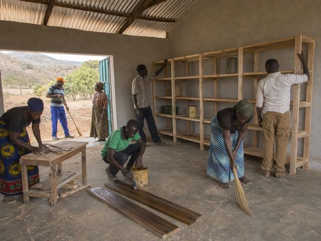 Local artisans and community members finish and seal the raised wooden shelving inside the Uwezo Project storage hall in Chepareria
